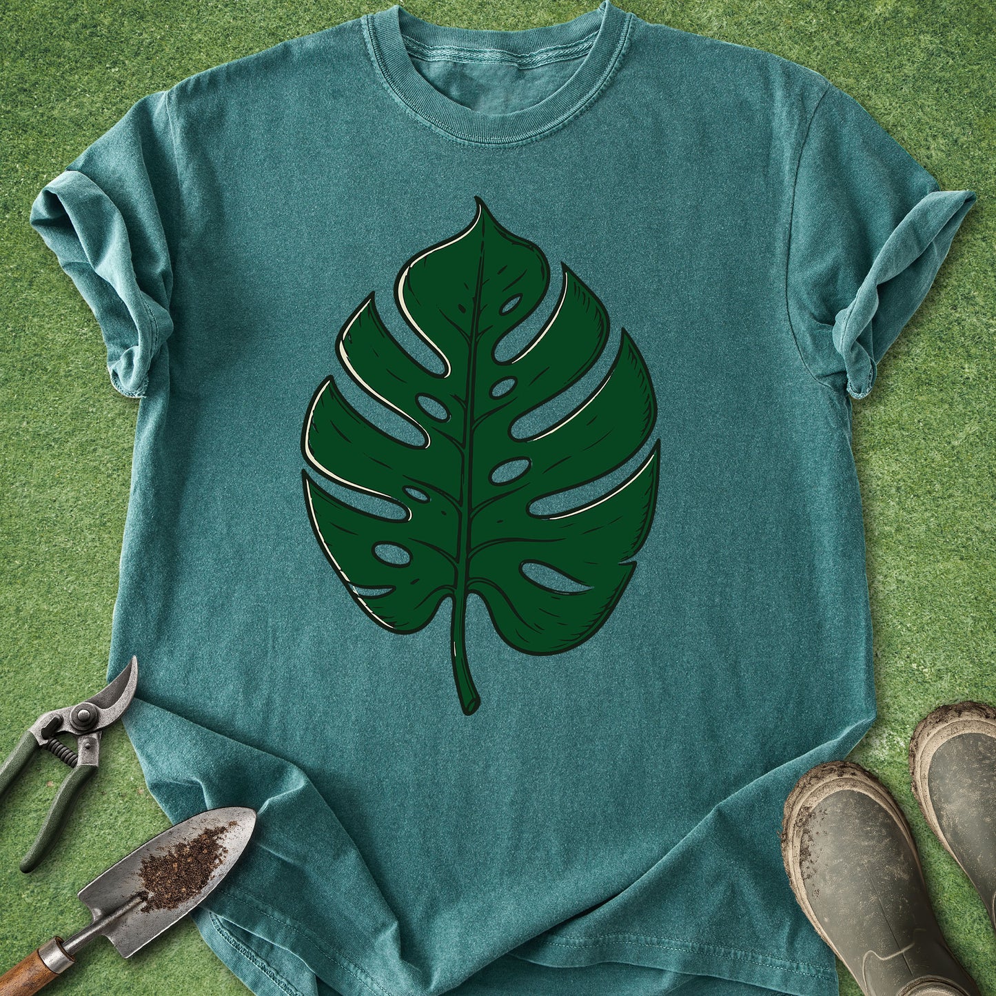 Teal t-shirt with a large green leaf design on a grassy background
