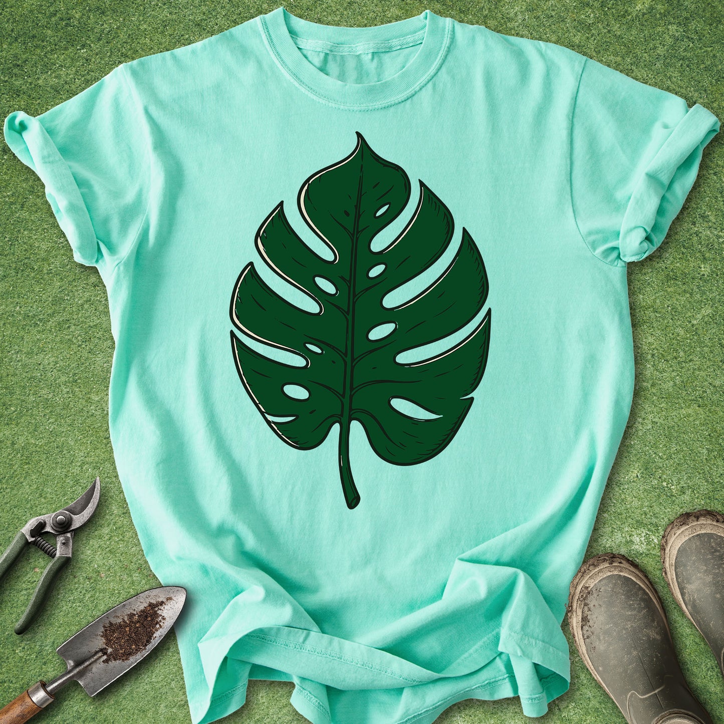 Mint green t-shirt with a large green leaf graphic on a grassy background.
