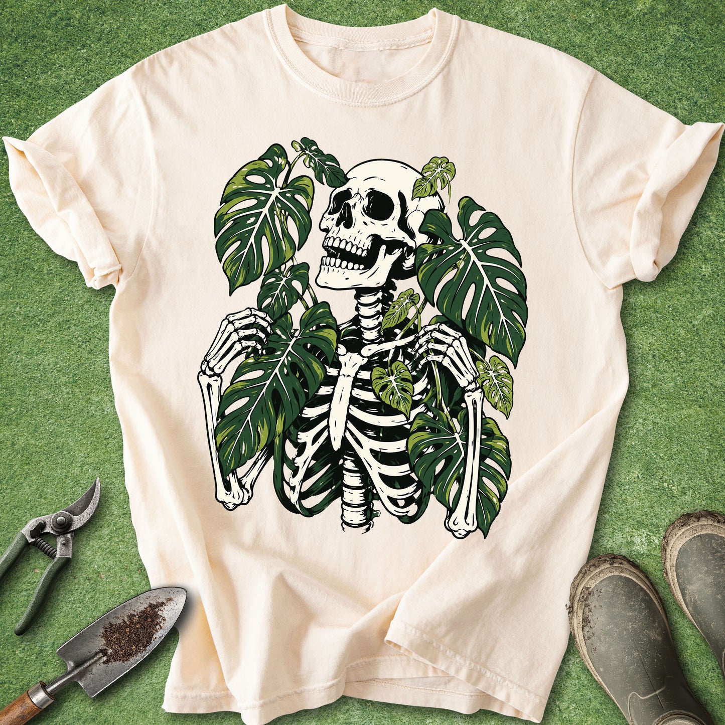Ivory t-shirt featuring a skeleton surrounded by large green Monstera leaves in a detailed gothic botanical illustration.
