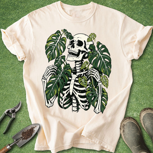 Ivory t-shirt featuring a skeleton surrounded by large green Monstera leaves in a detailed gothic botanical illustration.