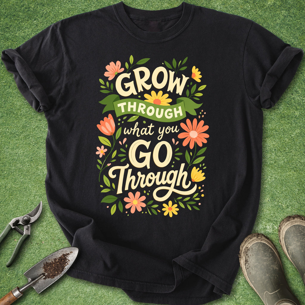 Black t-shirt with motivational quote on a green surface with gardening tools.