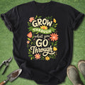 Black t-shirt with motivational quote on a green surface with gardening tools.