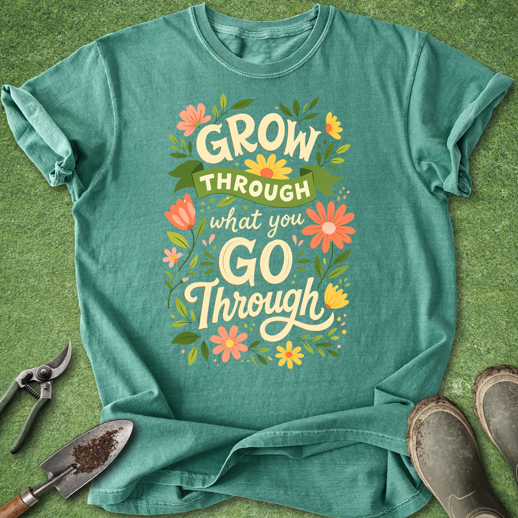 Teal t-shirt with motivational quote on a green background with gardening tools.