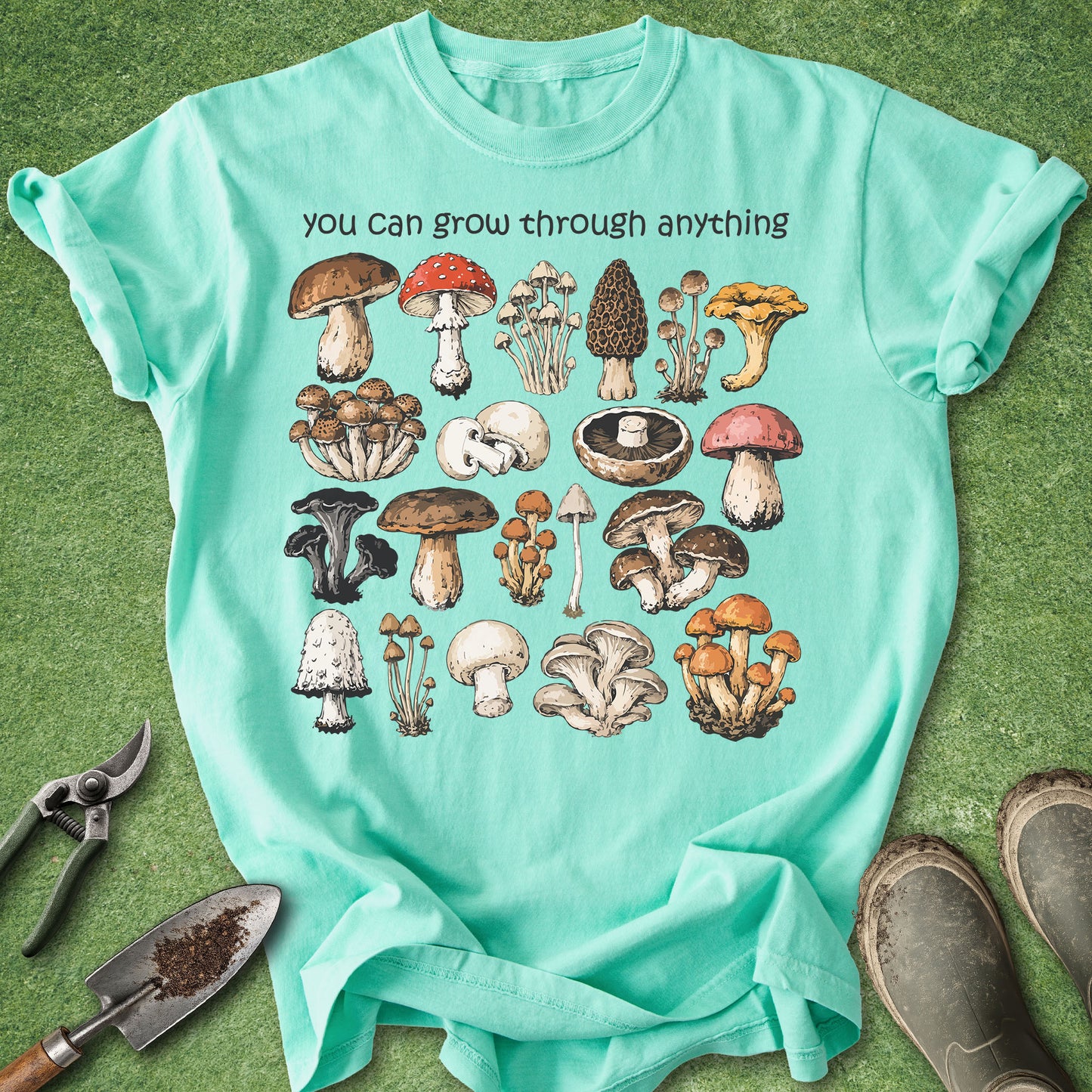 Mint green t-shirt with mushroom illustrations and text on a grass background