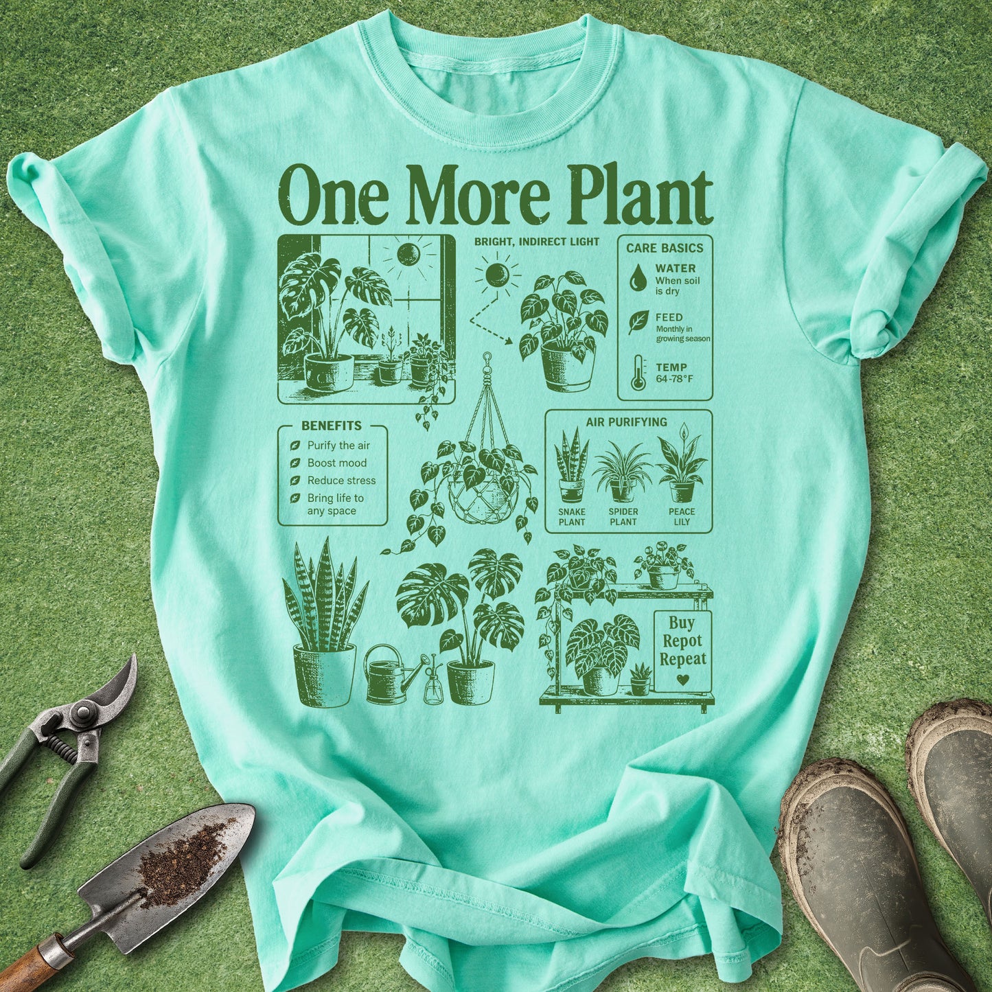 A mint green graphic t-shirt laid flat on a green grass-like surface, surrounded by gardening props including pruning shears, a small hand trowel, and muddy boots. The shirt features a dark green retro-style infographic titled 'One More Plant' with illustrations of potted plants, watering cans, a sun, and care tips.