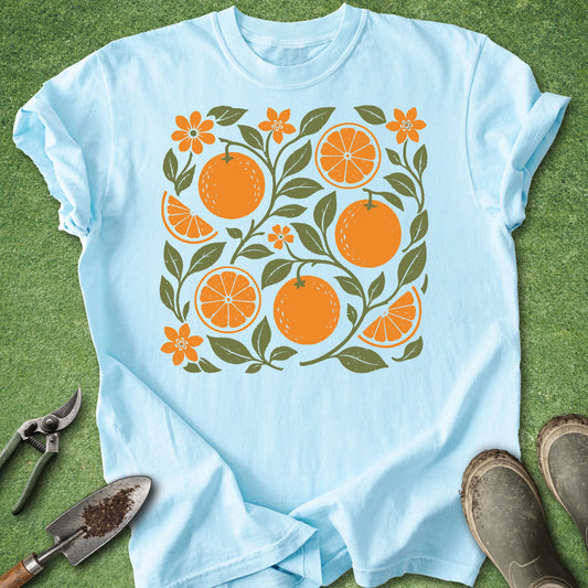 Light blue t-shirt featuring a vintage-style orange botanical design with whole oranges, citrus slices, orange blossoms and green leafy branches.