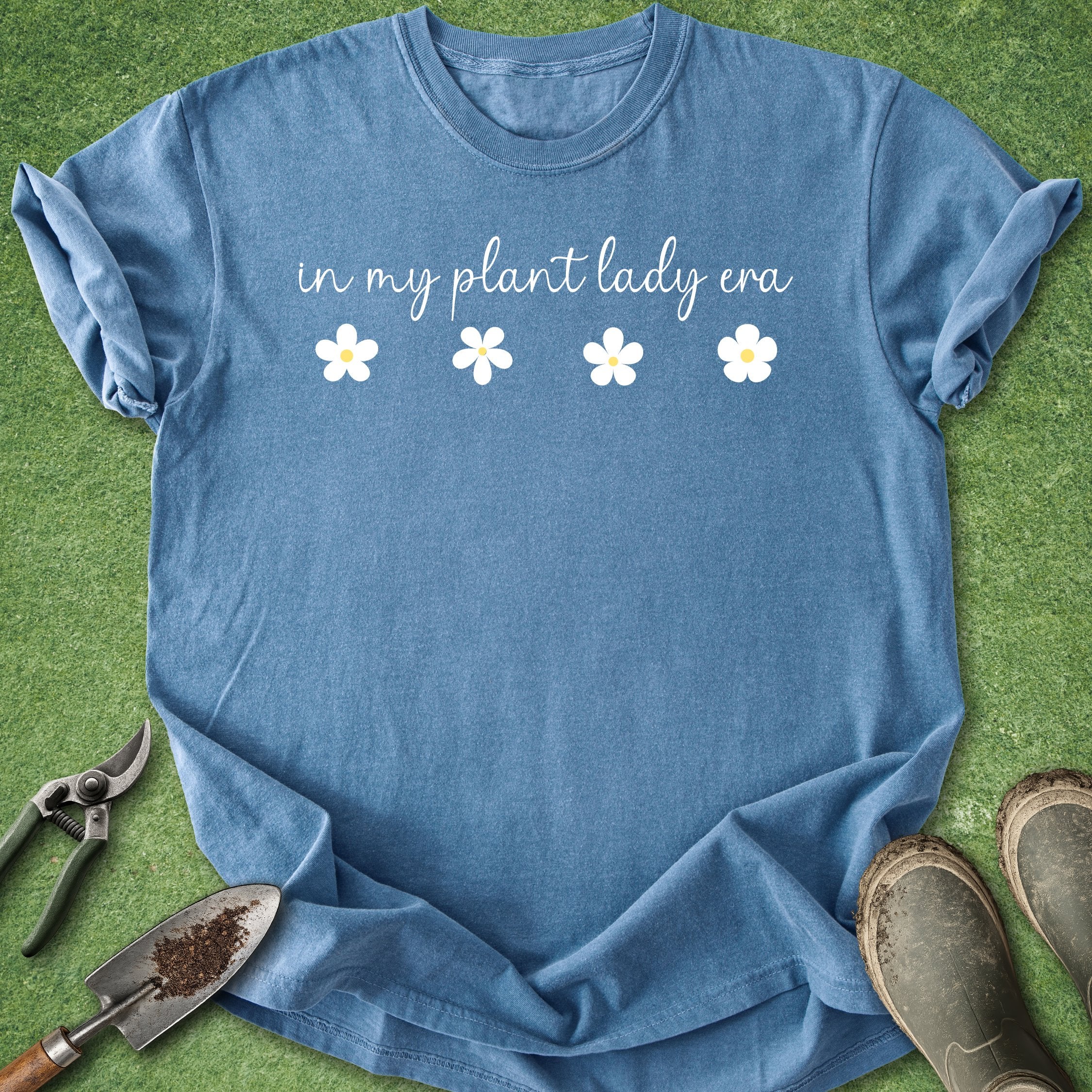 Blue t-shirt with 'in my plant lady era' text and flowers on a grass background