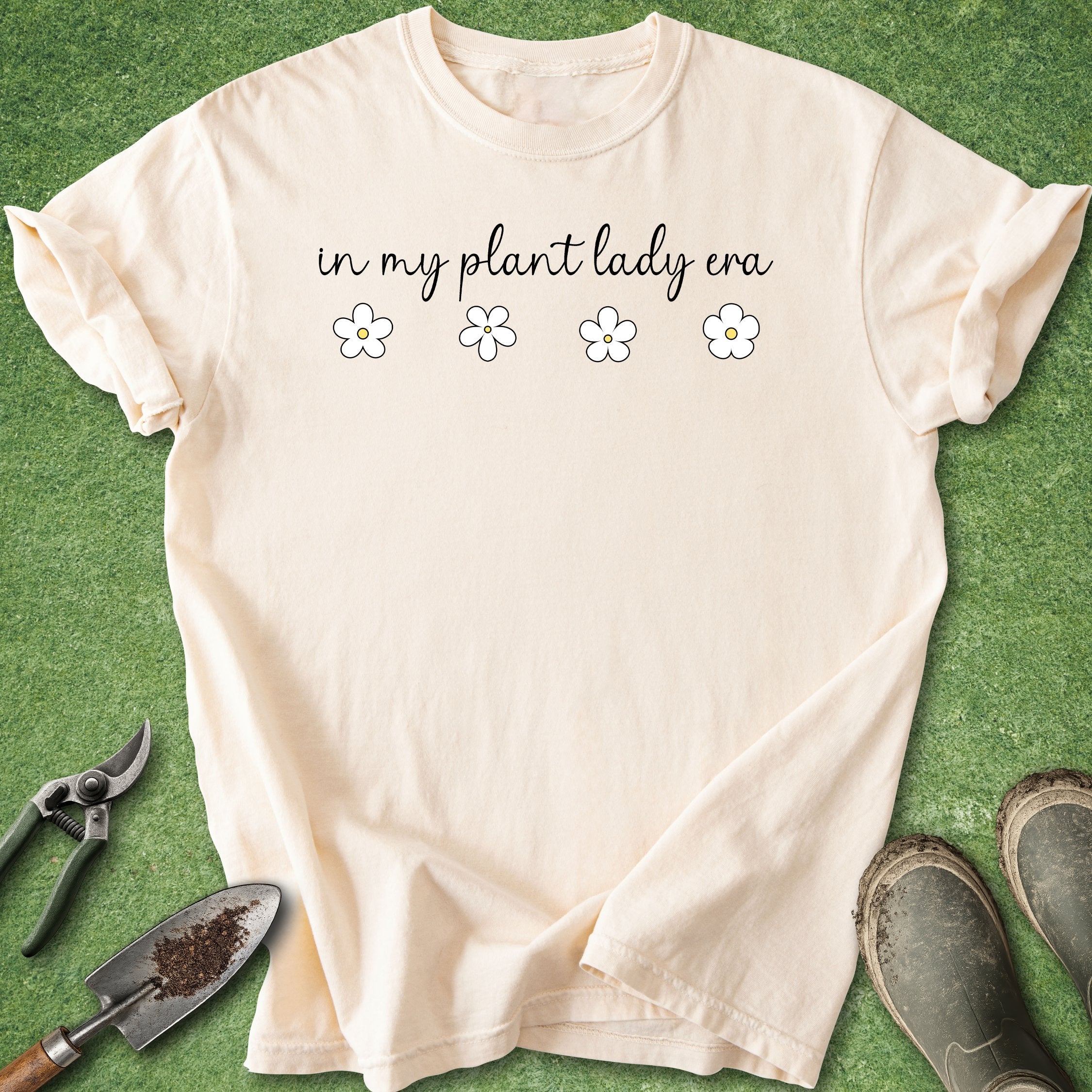 Beige t-shirt with 'in my plant lady era' text on a green background with gardening tools.
