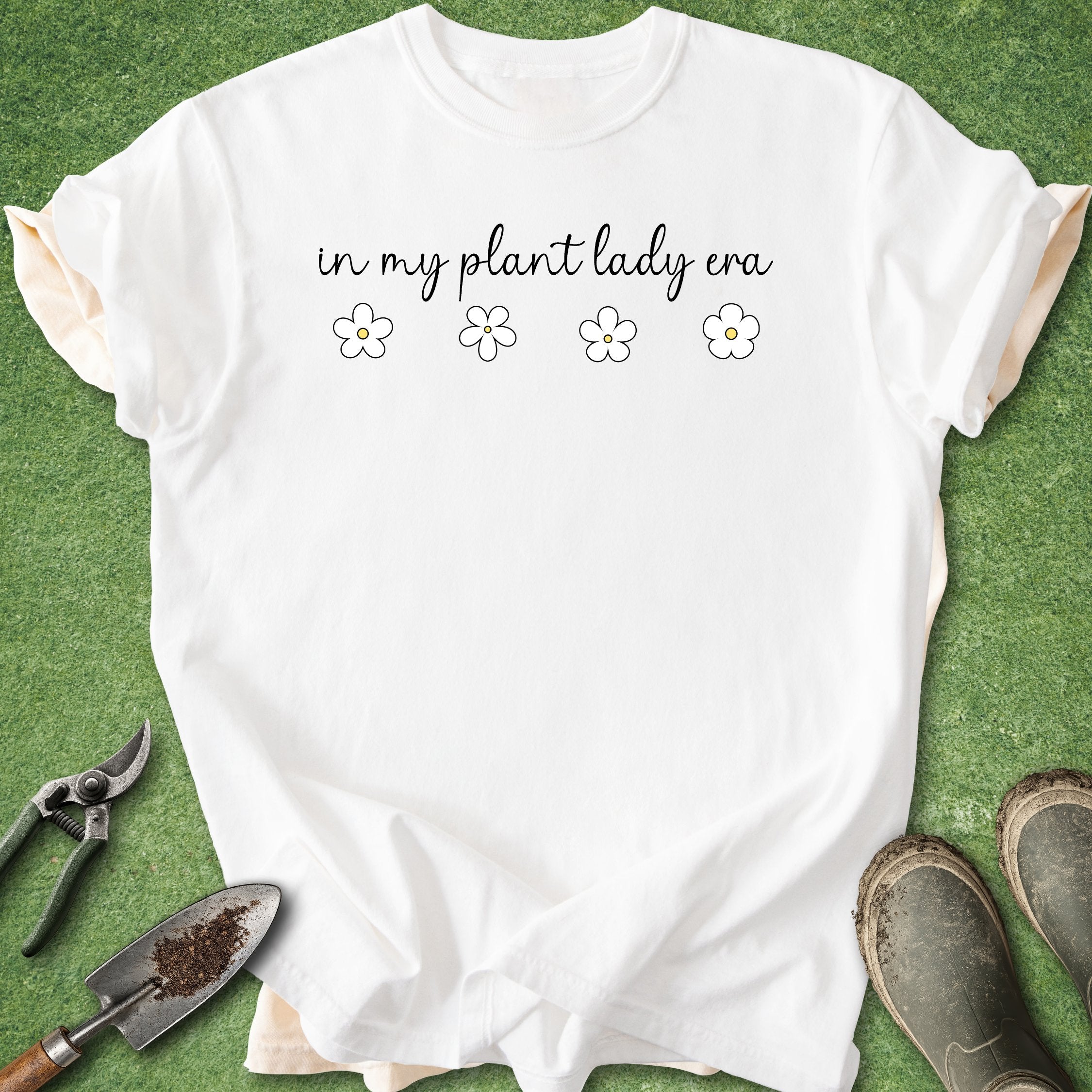 White t-shirt with 'in my plant lady era' text on a green background with gardening tools.