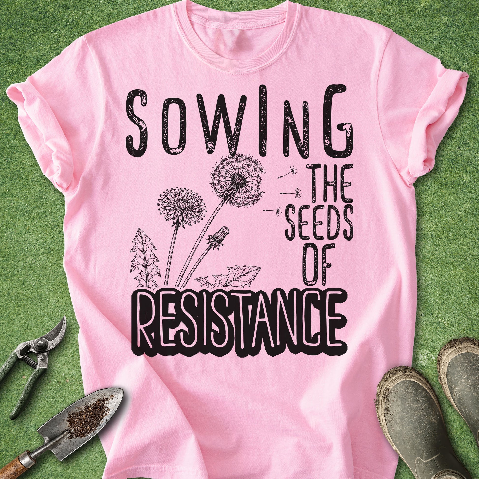 Pink t-shirt with 'Sowing the Seeds of Resistance' text and dandelion graphics on a green background.