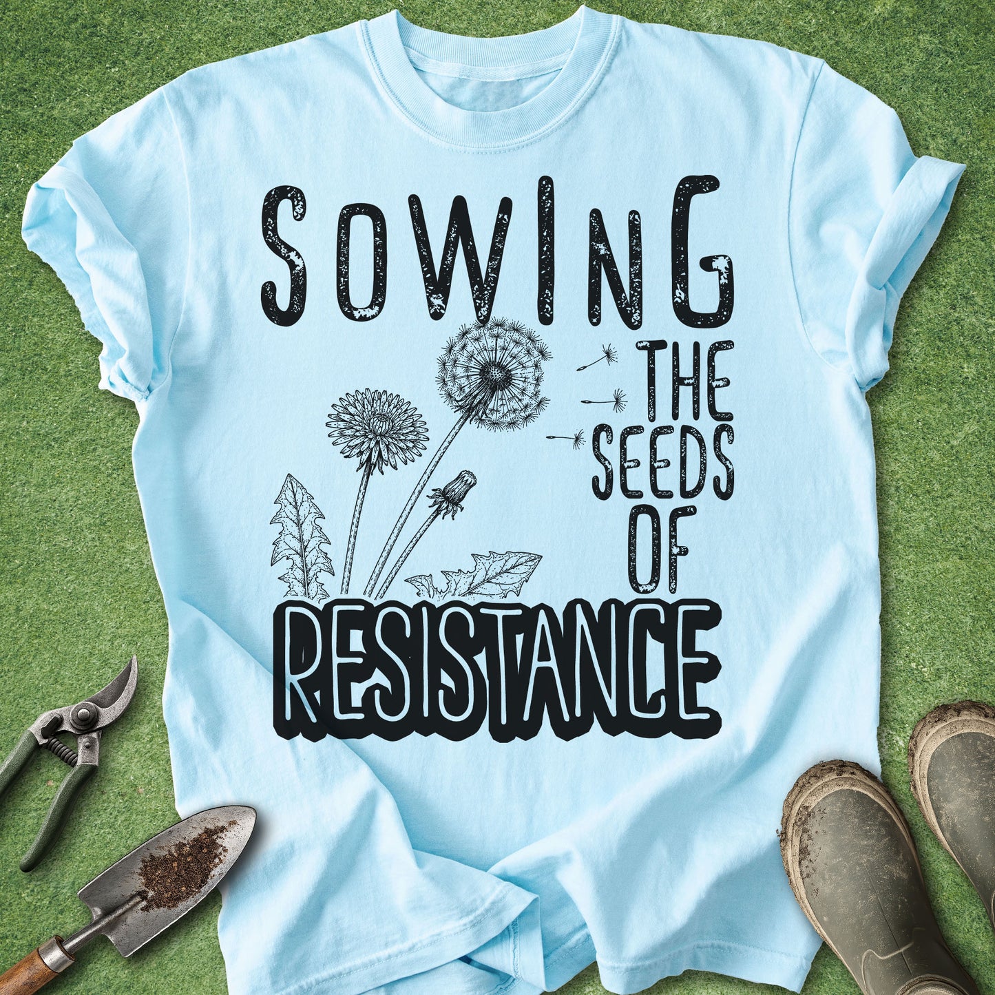 Light blue t-shirt with 'Sowing the Seeds of Resistance' text on a green background with gardening tools.