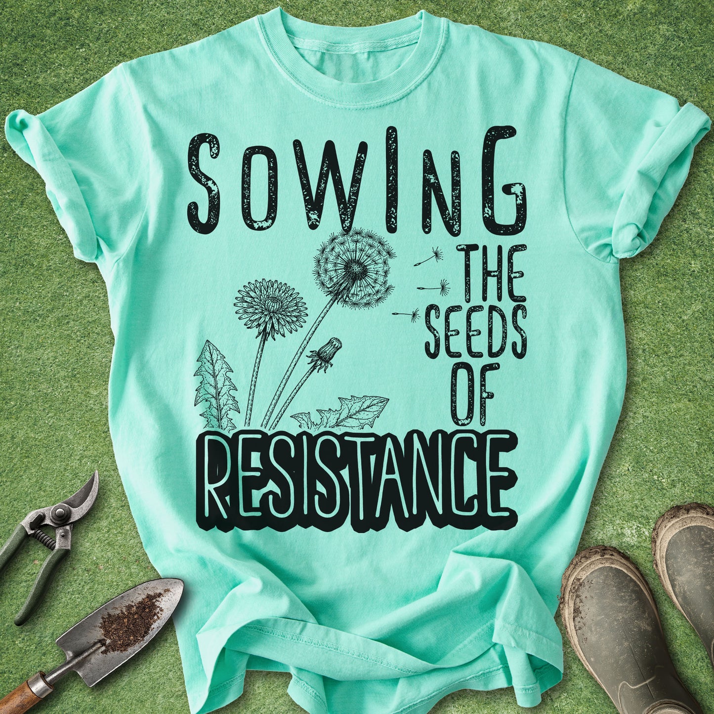 Mint green t-shirt with 'Sowing the Seeds of Resistance' text on a grass background.