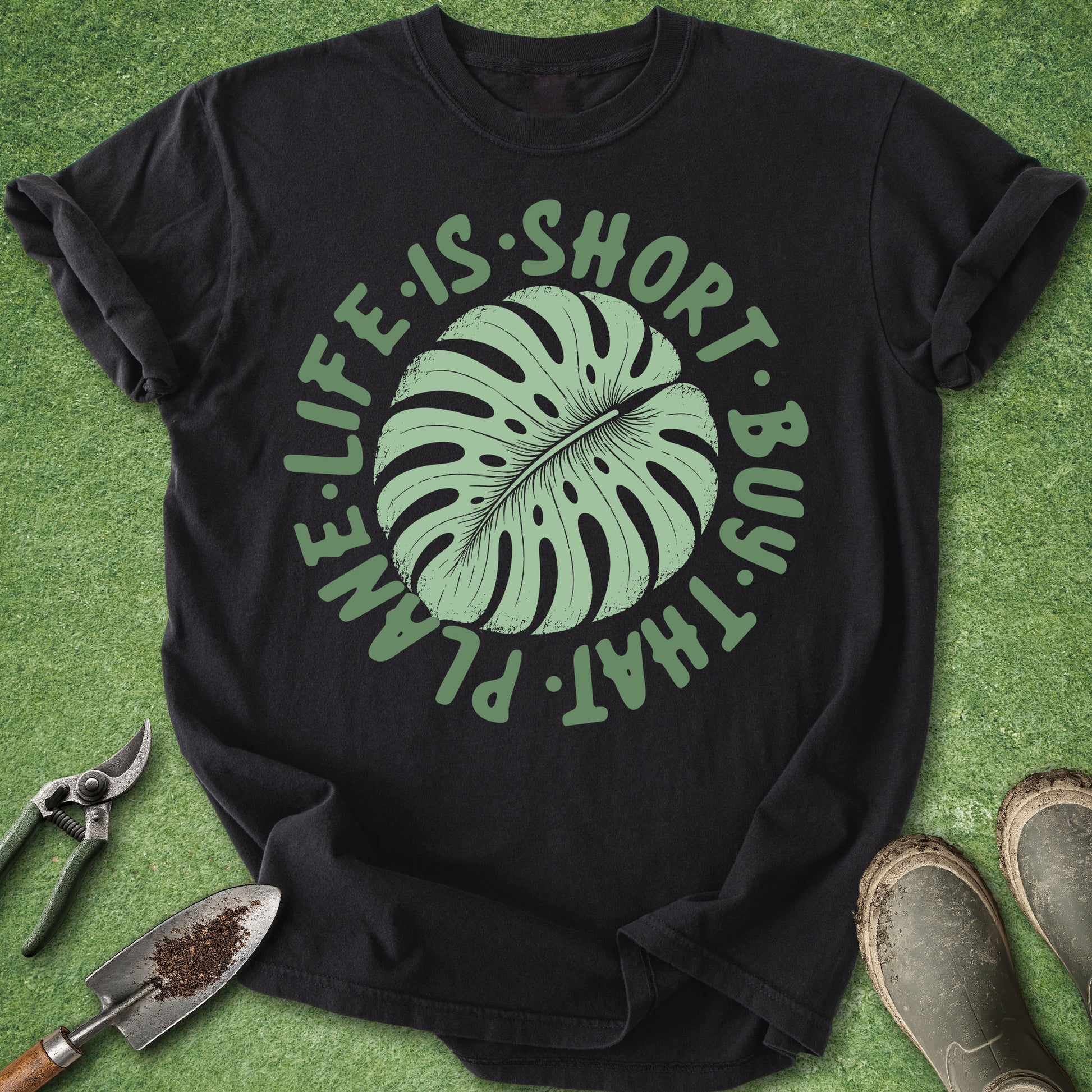 Black t-shirt with green leaf graphic and text on a grass background