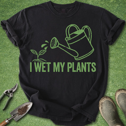 Black t-shirt with green graphic and text 'I Wet My Plants' on a grass background