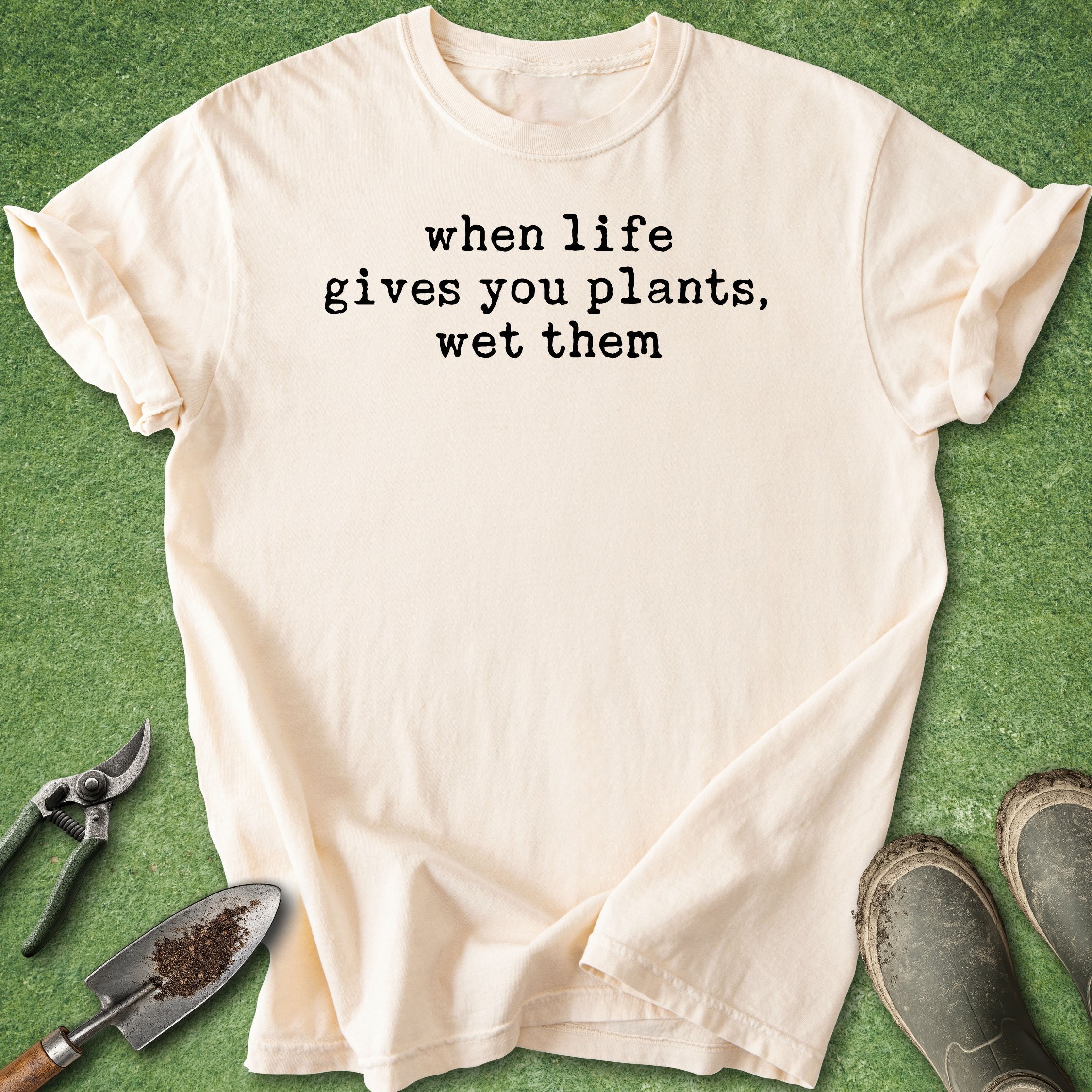Beige t-shirt with humorous text on a green background with gardening tools.