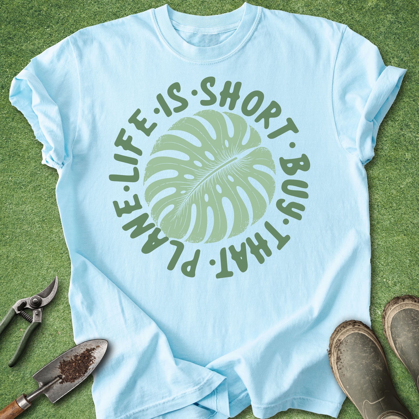 Light blue t-shirt with green leaf graphic and text on a grass background