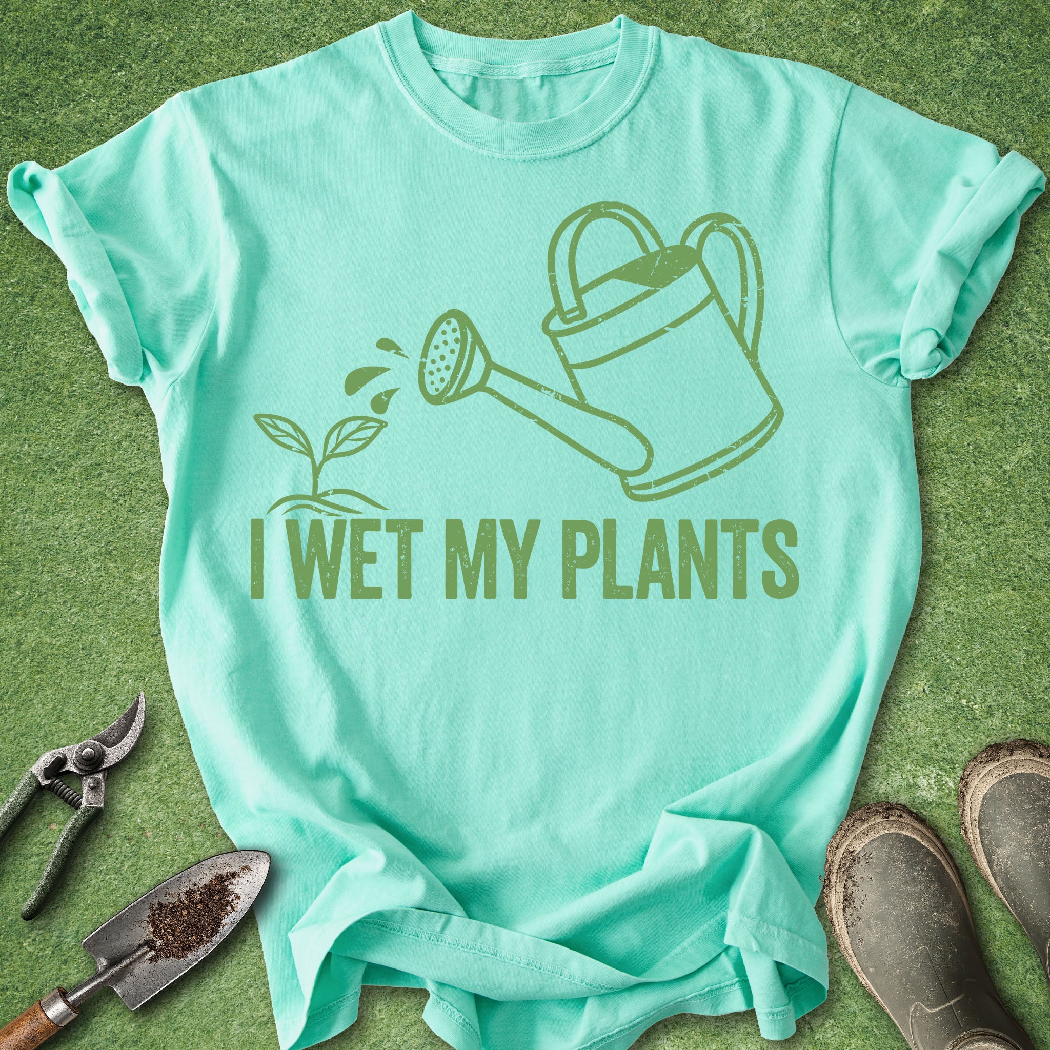 Mint green t-shirt with gardening-themed design and tools on a grass background