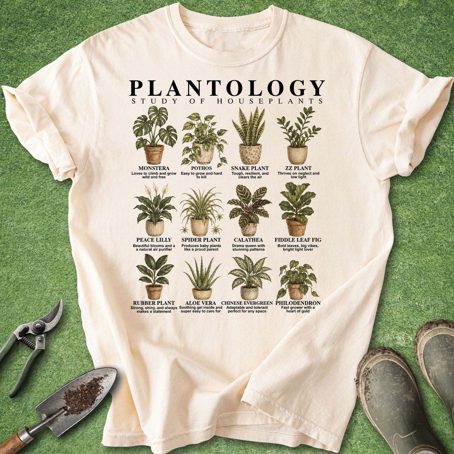A cream-colored graphic t-shirt laid flat on a green grass-like surface, surrounded by gardening props including pruning shears, a trowel, and work boots. The shirt features a detailed educational chart titled 'PLANTOLOGY: STUDY OF HOUSEPLANTS' with illustrations of various houseplants and their common names.