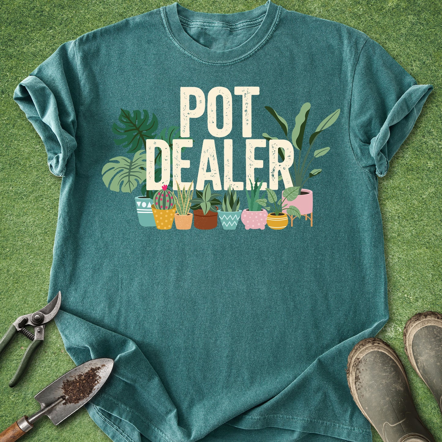 Blue Spruce Comfort Colors t-shirt featuring the phrase "Pot Dealer" above colorful illustrated potted houseplants including monstera, snake plants, cactus, and tropical foliage in decorative planters.