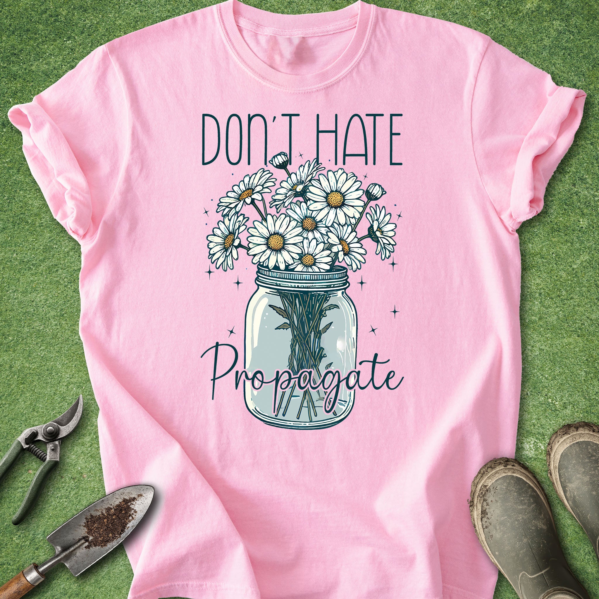 Pink t-shirt with a graphic of flowers in a jar and text 'Don't Hate Propagate' on a green background.