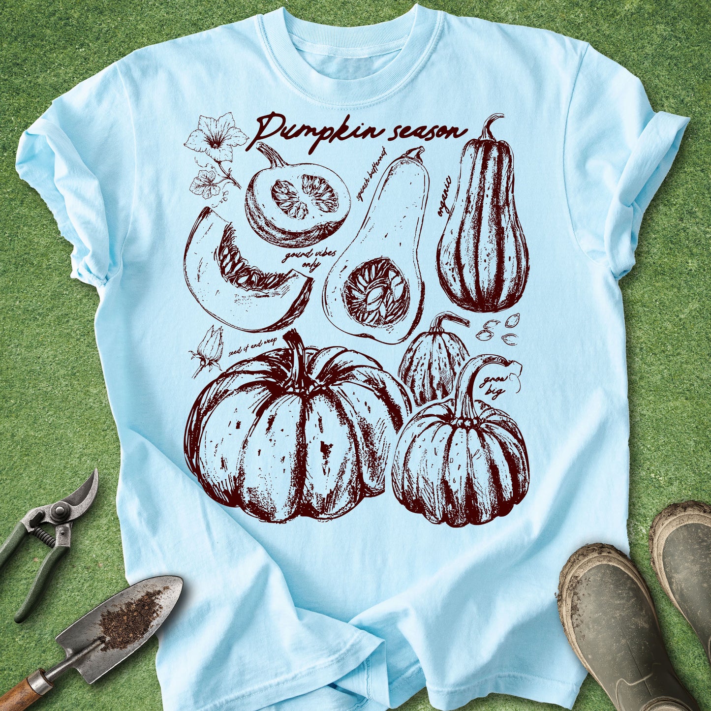 Light blue t-shirt with pumpkin season graphic on a green grass background