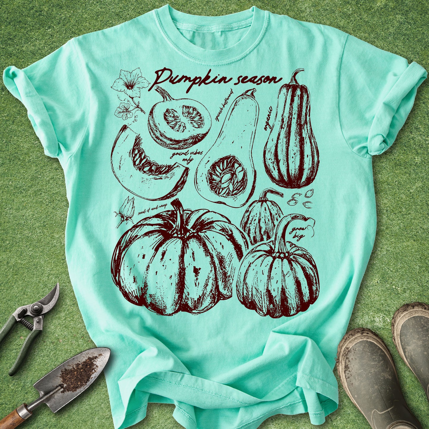 Mint green t-shirt with pumpkin season graphic on a grass background