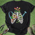 Black t-shirt with a colorful skeleton and flowers design on a green grass background.