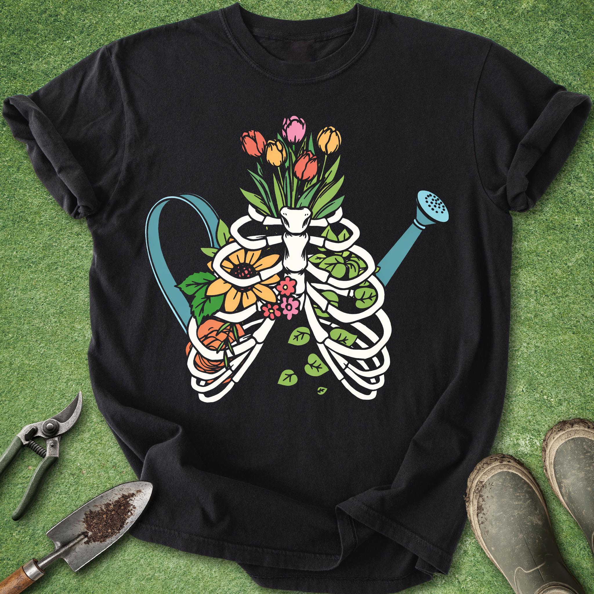 Black t-shirt with a colorful skeleton and flowers design on a green grass background.