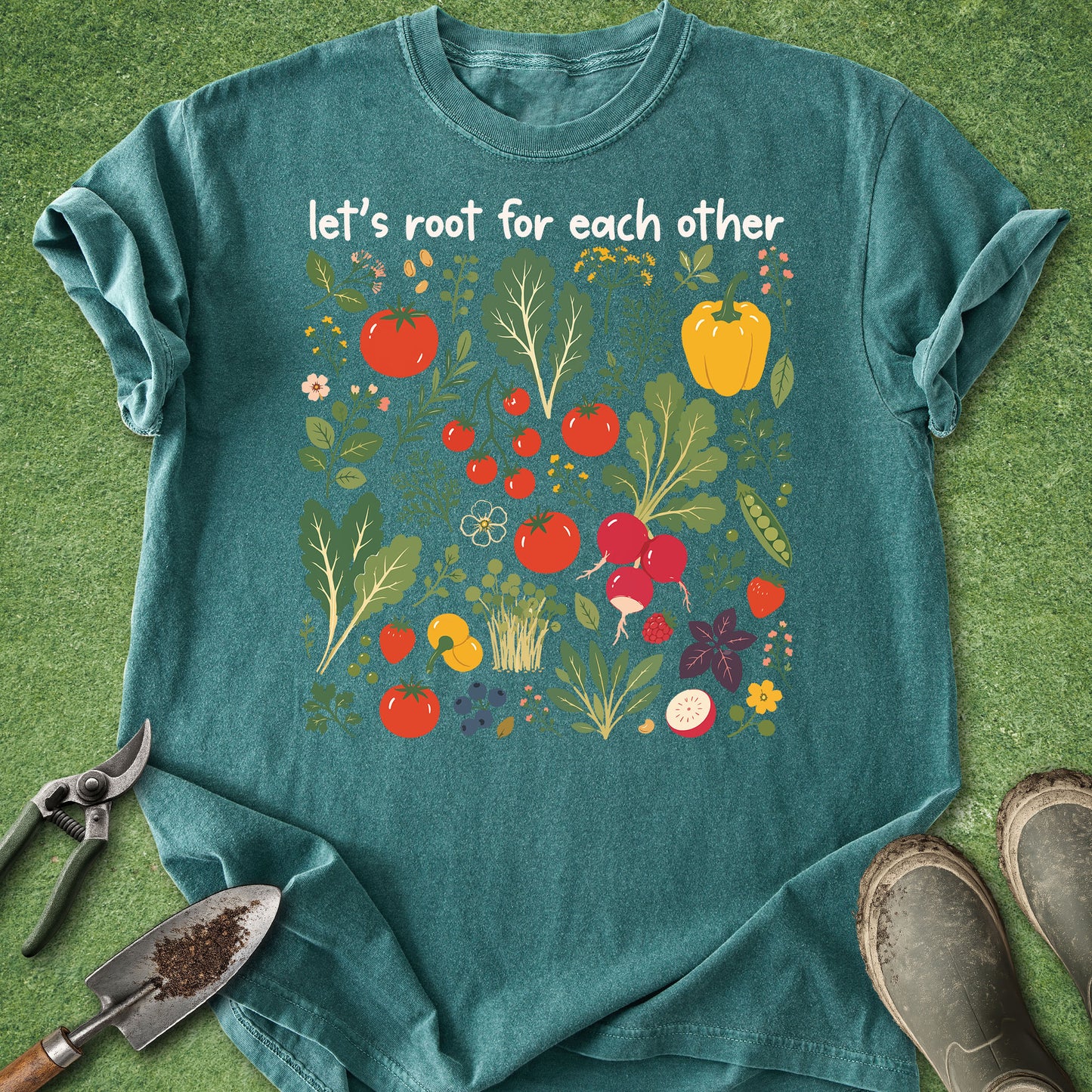 Teal t-shirt with vegetable design and text 'let's root for each other' on a grass background
