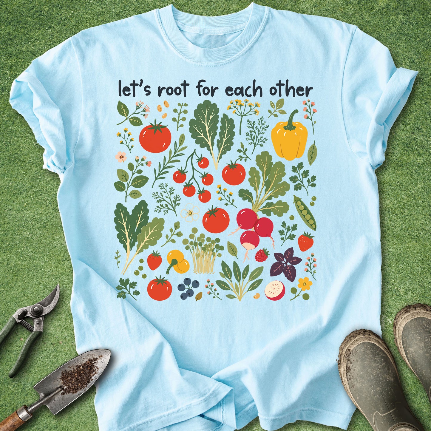 Light blue t-shirt with garden-themed design and text 'let's root for each other' on a grass background.