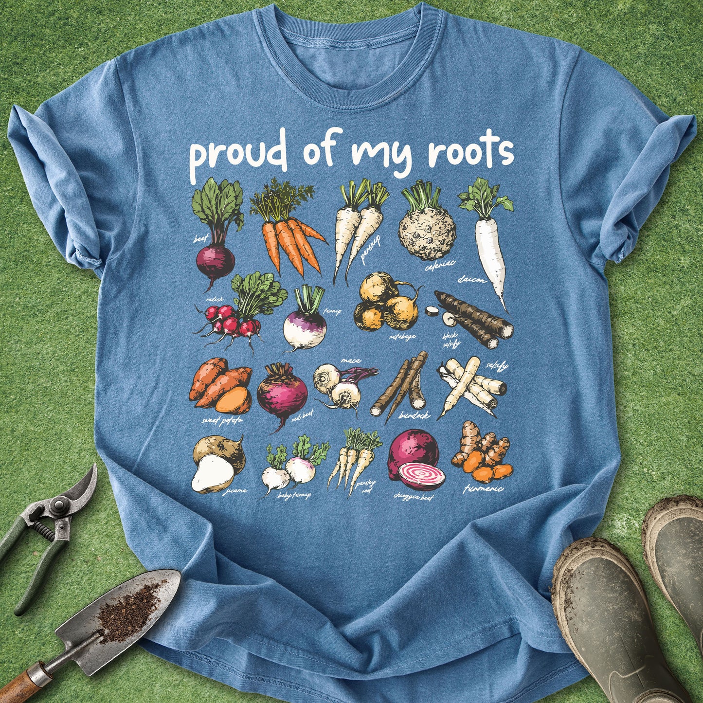 Blue t-shirt with vegetable illustrations and 'proud of my roots' text on a grass background.