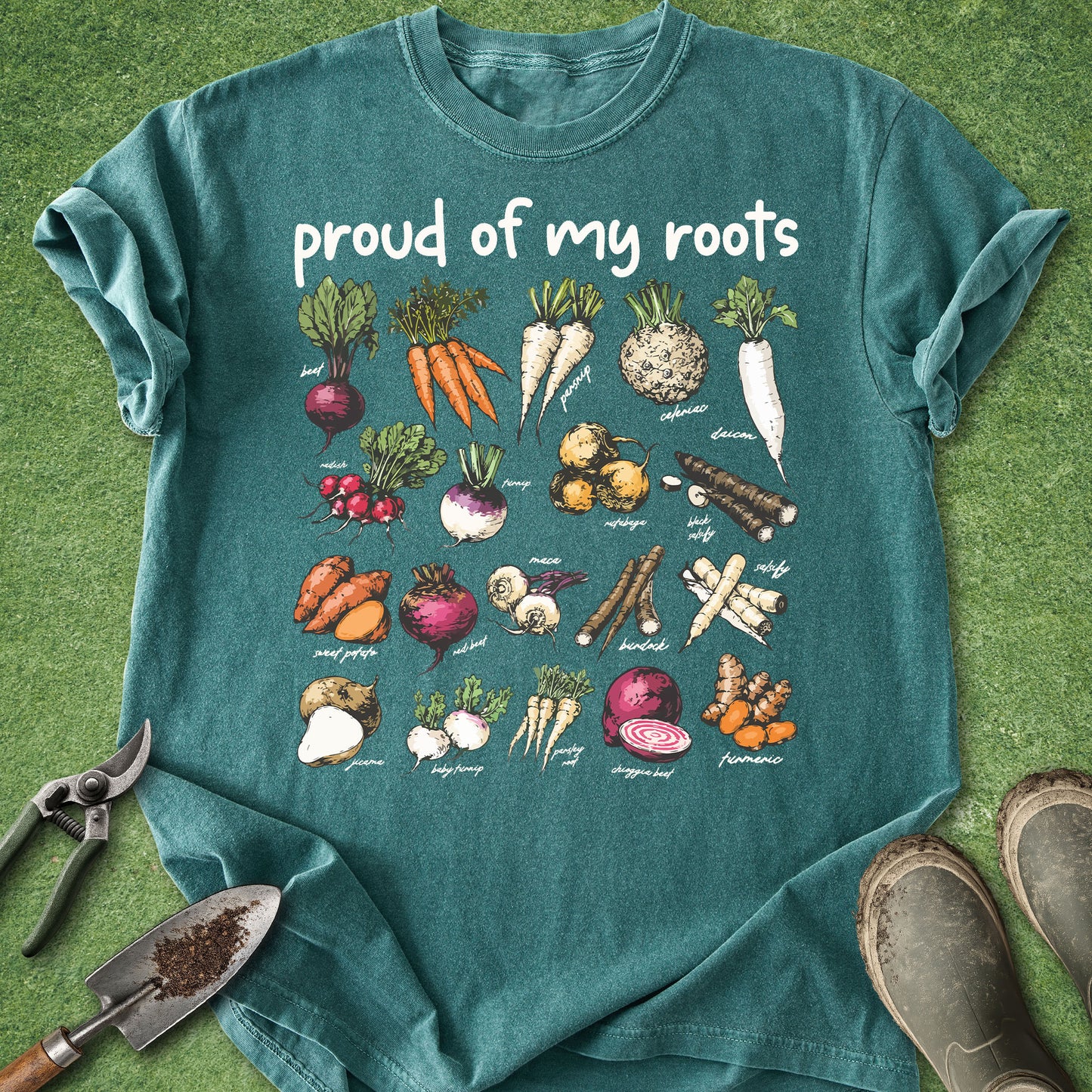 Teal t-shirt with vegetable illustrations and 'proud of my roots' text on a grass background