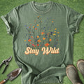 Green t-shirt with 'Stay Wild' text and floral design on a grass background