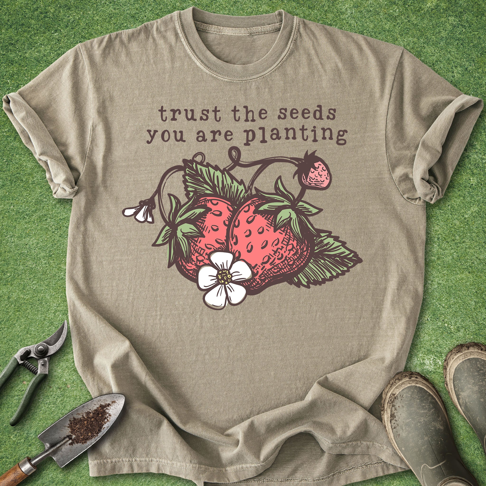 Beige t-shirt with strawberry graphic and 'trust the seeds you are planting' text on a green background