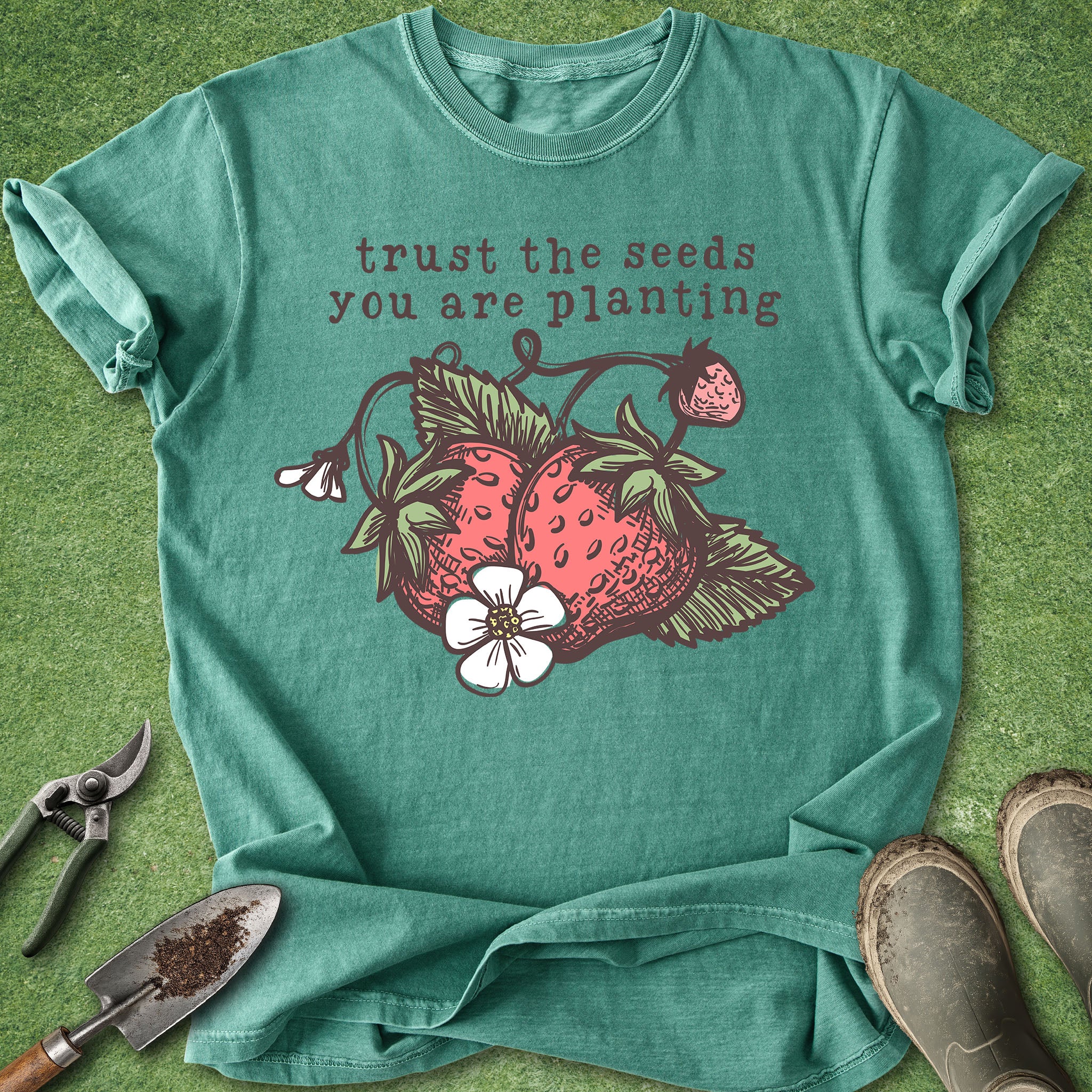 Teal t-shirt with strawberry graphic and text 'trust the seeds you are planting' on a green background.