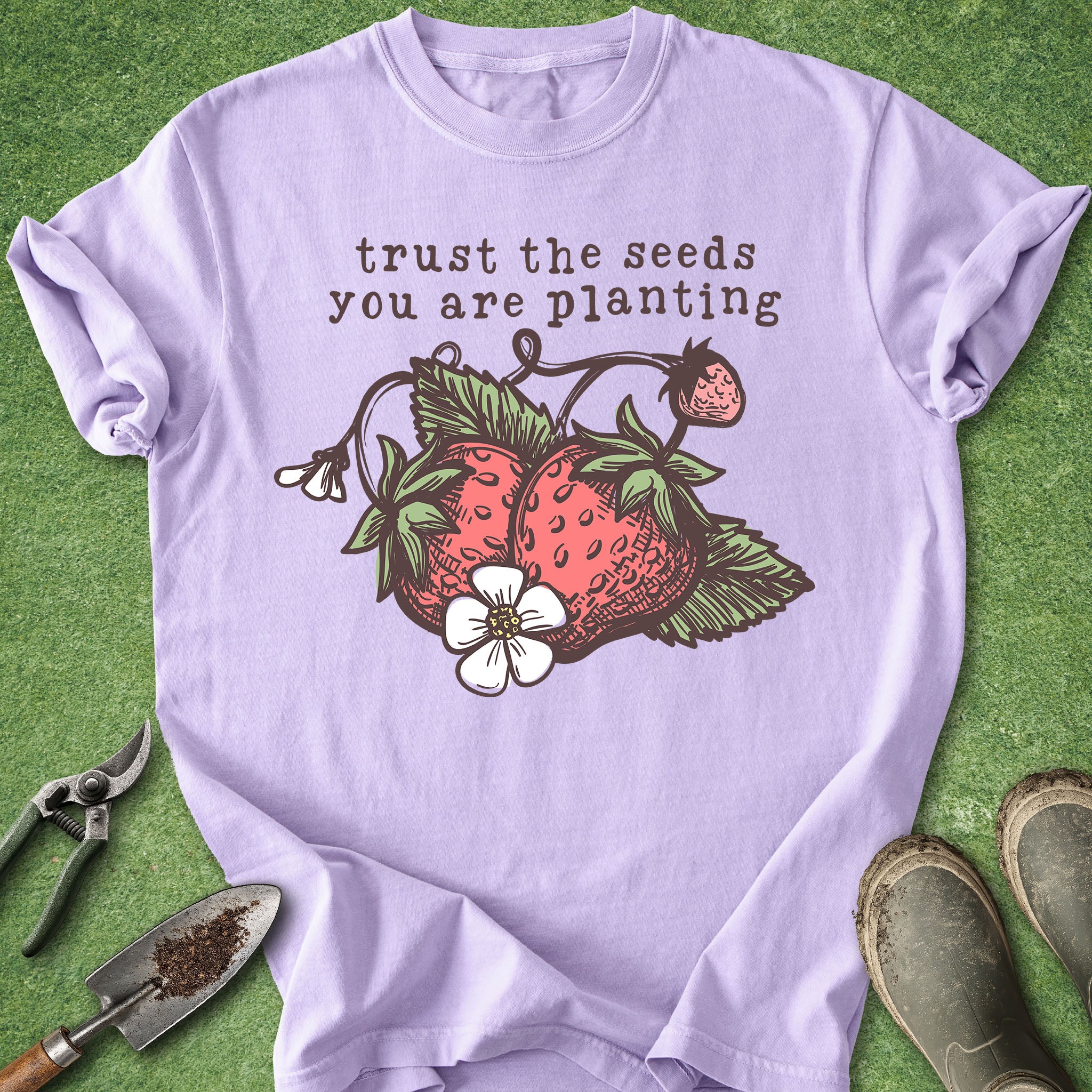 Purple t-shirt with strawberry graphic and text 'trust the seeds you are planting' on a green background.