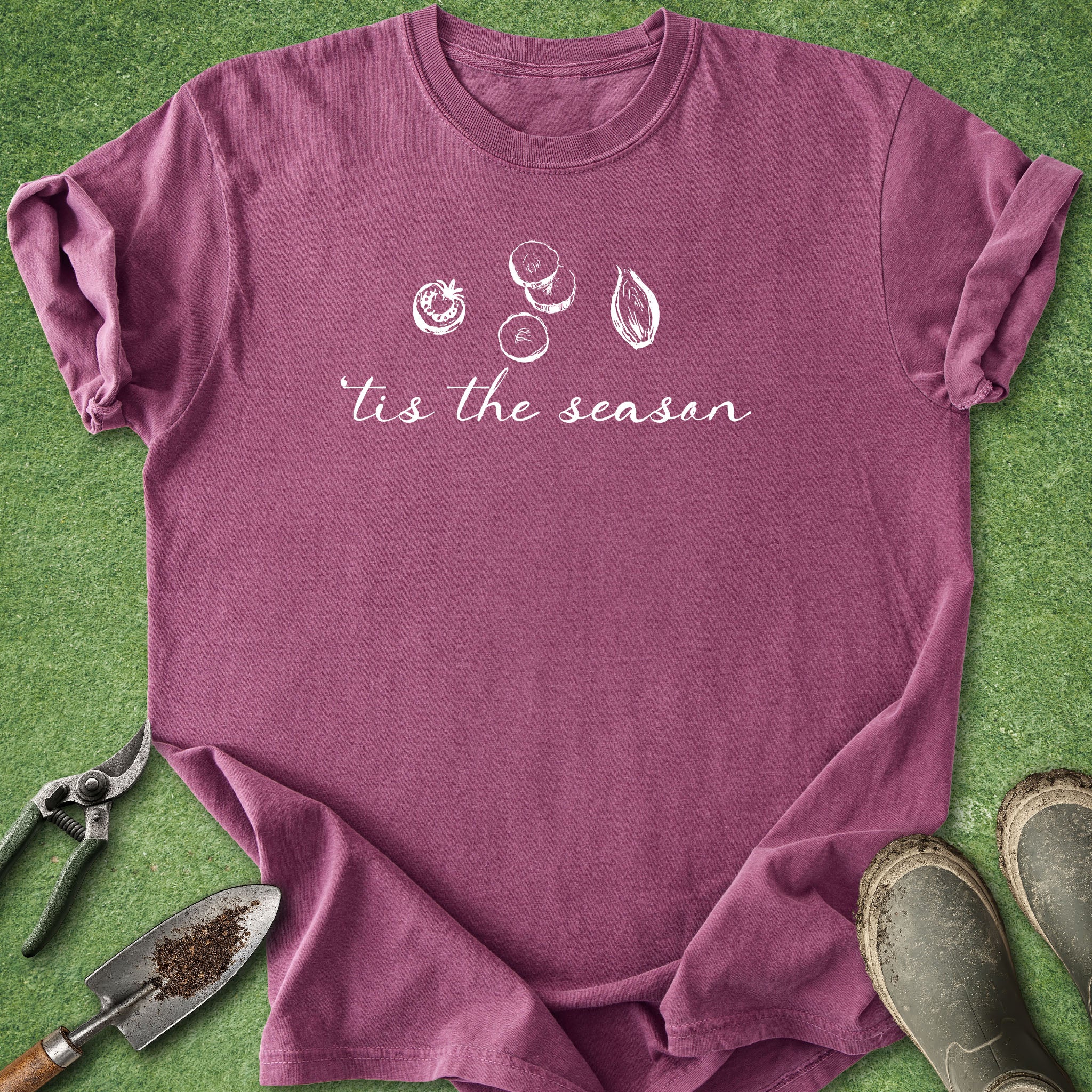 Purple t-shirt with 'tis the season' text and fruit illustrations on a green background with gardening tools and boots.