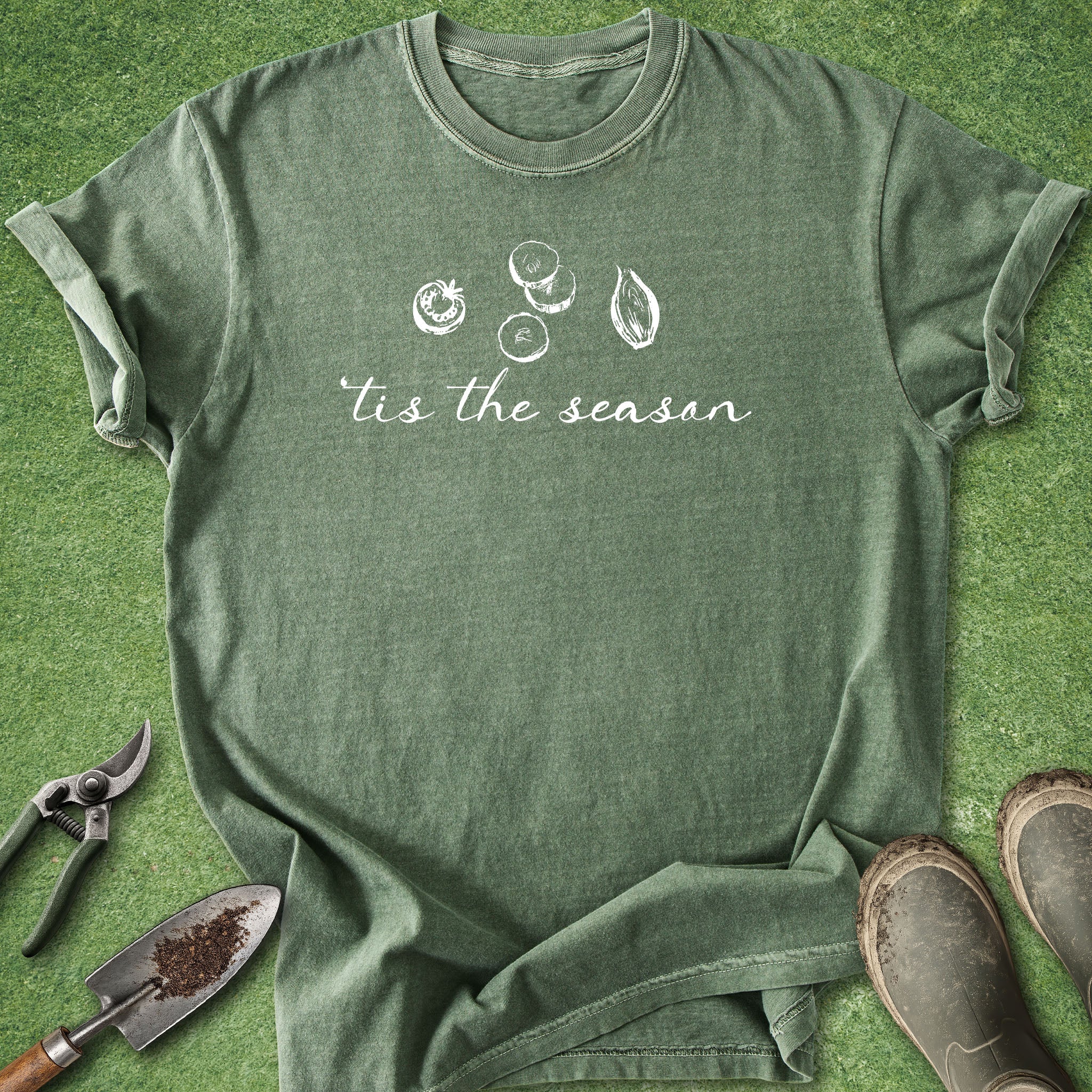 Green t-shirt with 'tis the season' text and gardening tools on a grass background