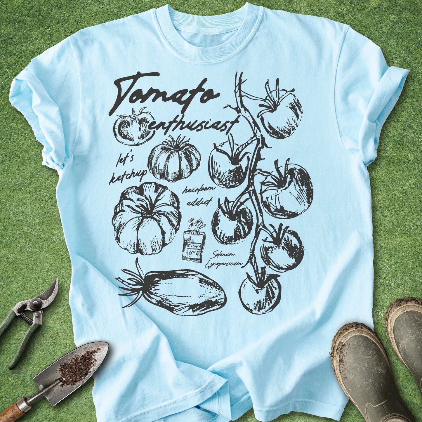Light blue t-shirt with tomato-themed design on a grass background