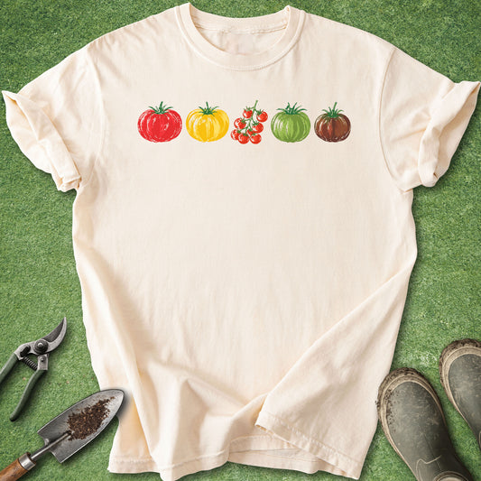 Ivory t-shirt featuring five illustrated tomato varieties in red, yellow, cherry, green and dark heirloom colors arranged in a simple horizontal row.