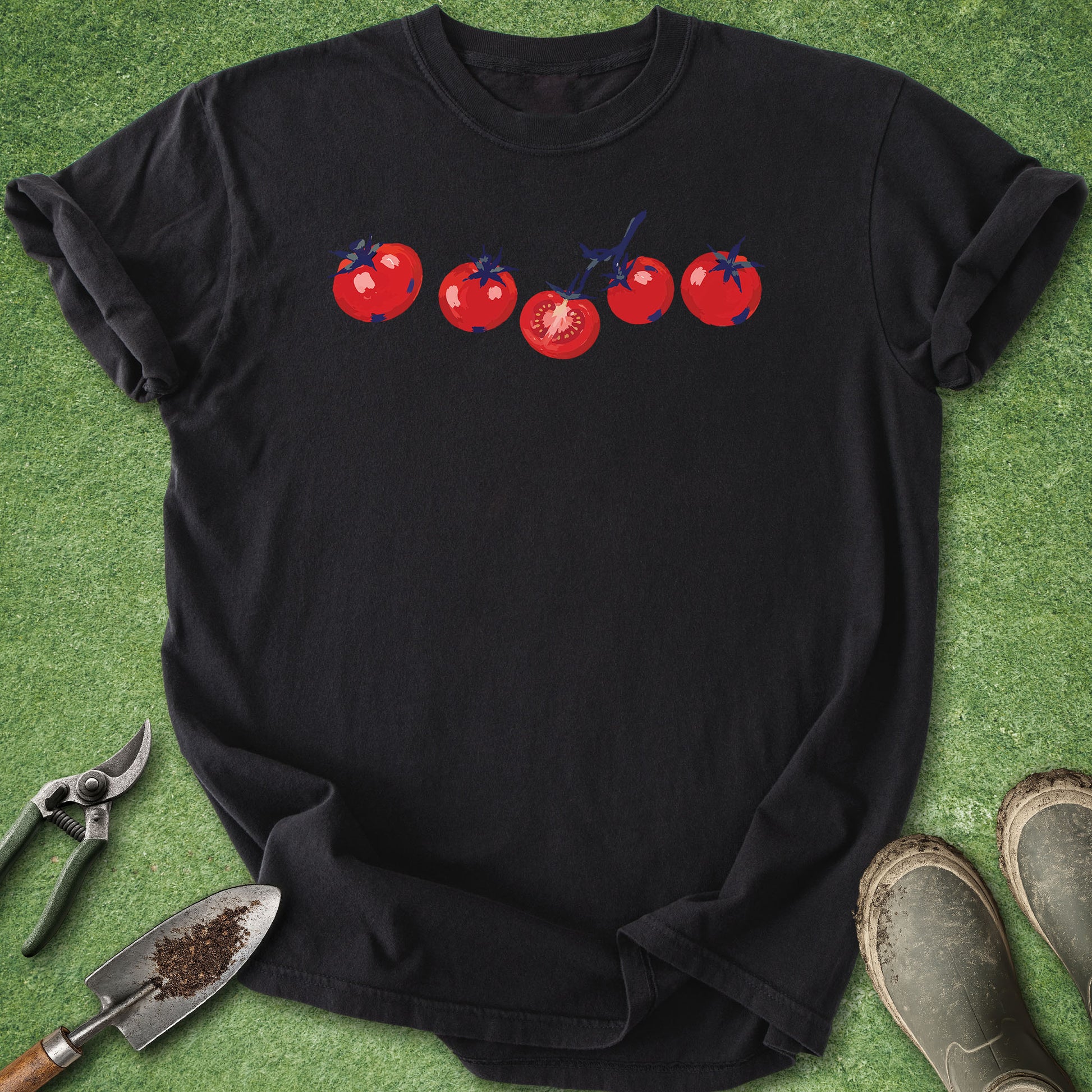 Black t-shirt with red tomato graphic on a green surface with gardening tools.