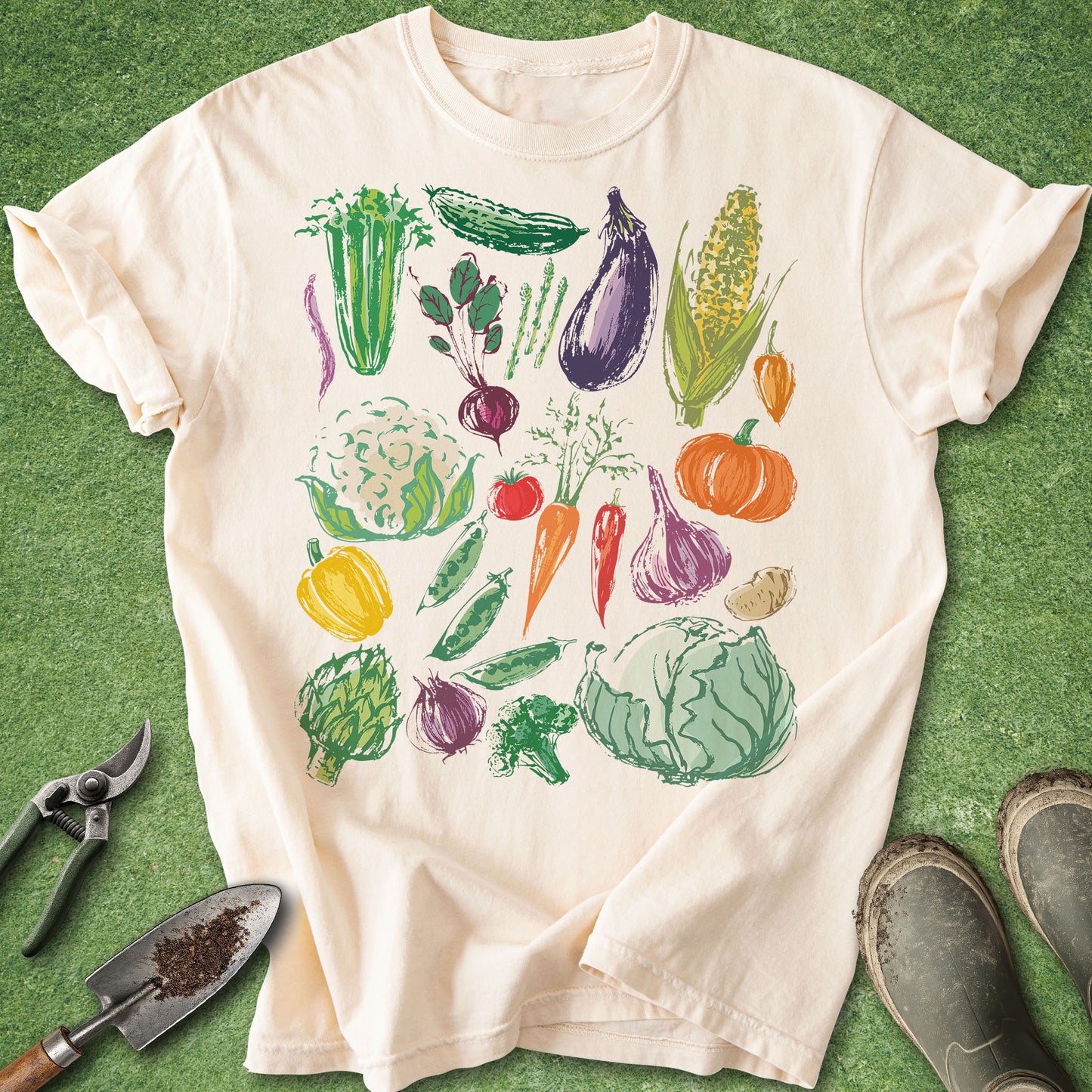 Ivory t-shirt with colorful hand-drawn vegetable illustrations including carrots, cabbage, corn, eggplant, and tomatoes arranged in a garden-inspired design