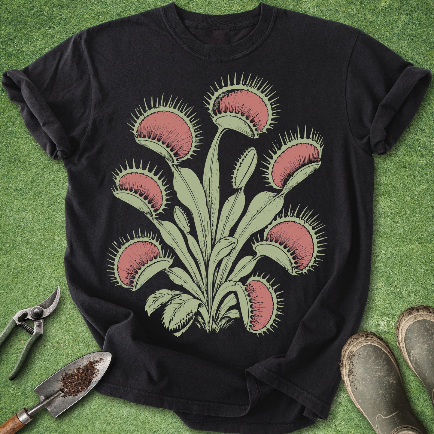 Black t-shirt with Venus flytrap design on a green surface with gardening tools.