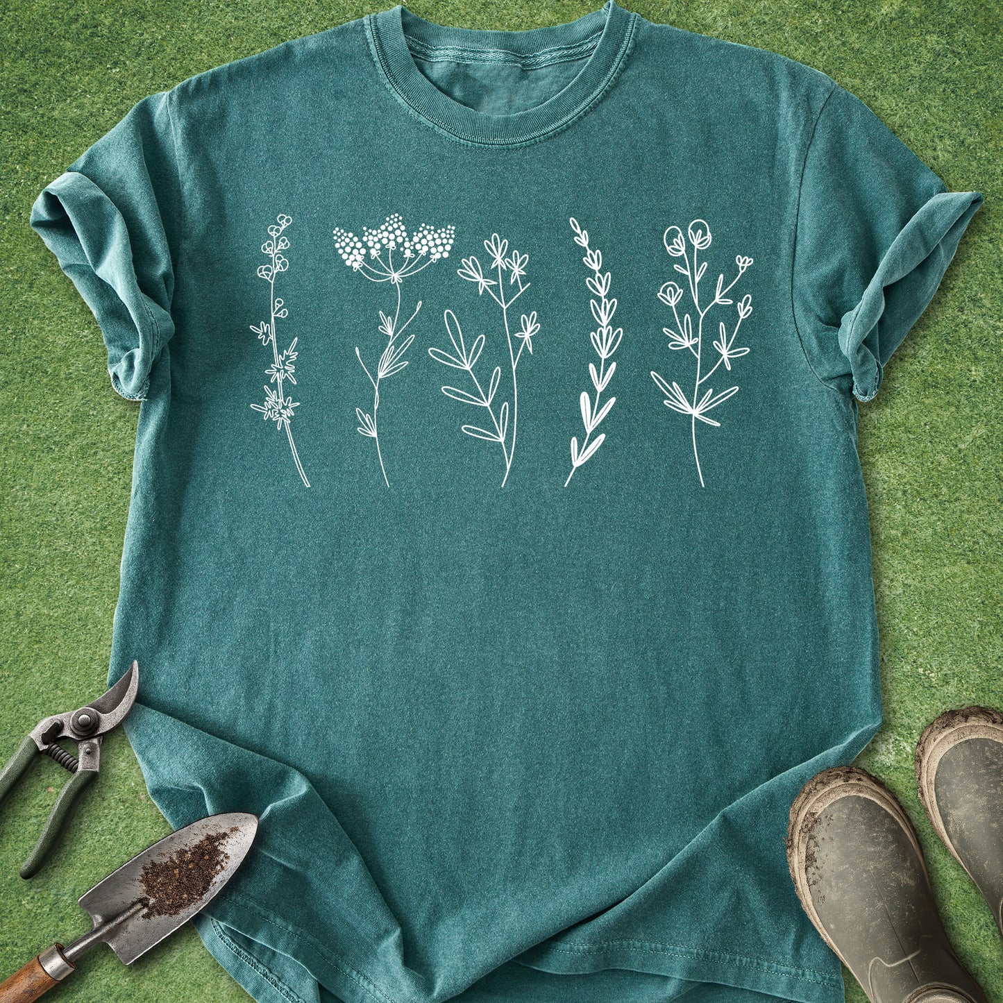 Teal t-shirt with white floral designs on a green grass background