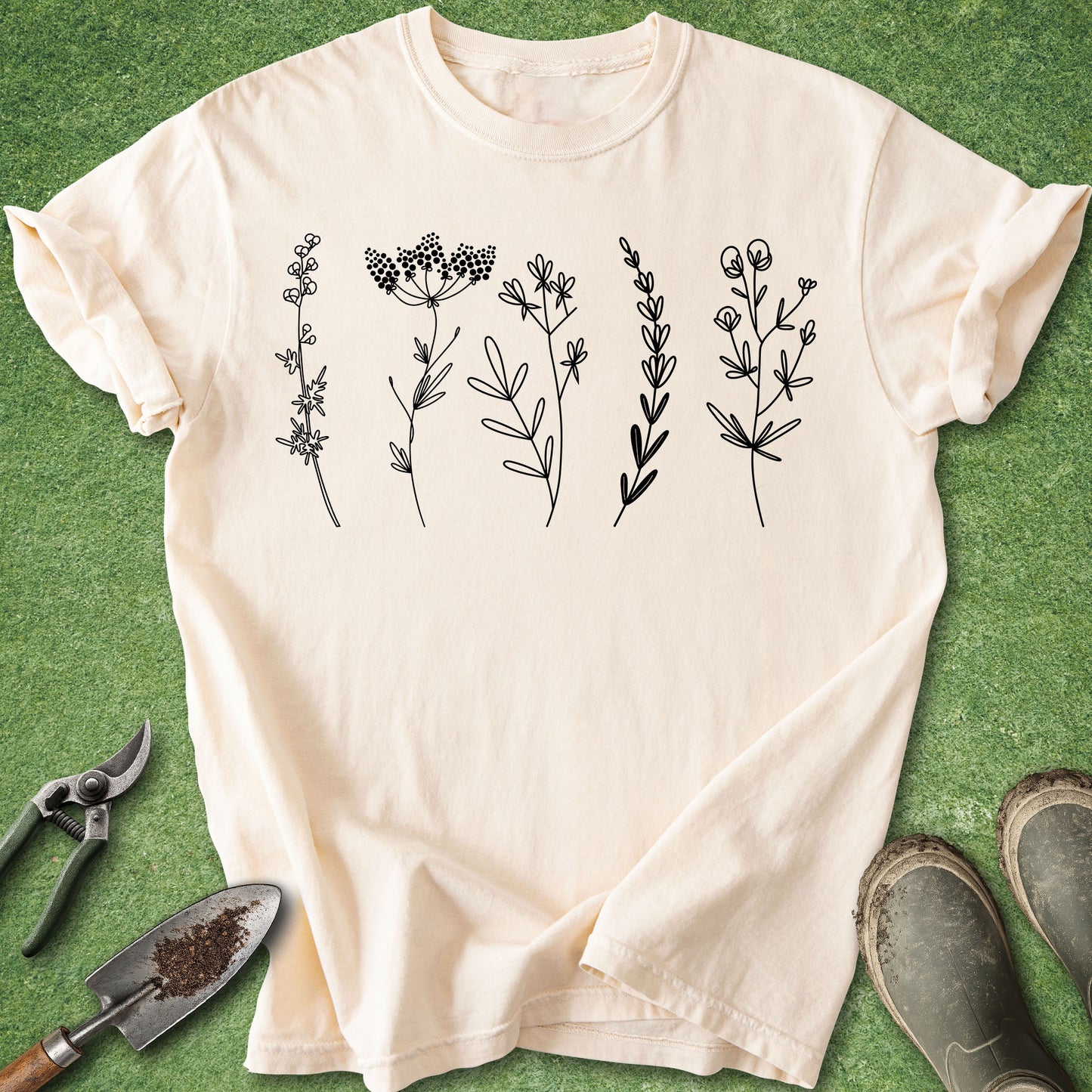 Beige t-shirt with black botanical illustrations on a green background with gardening tools.