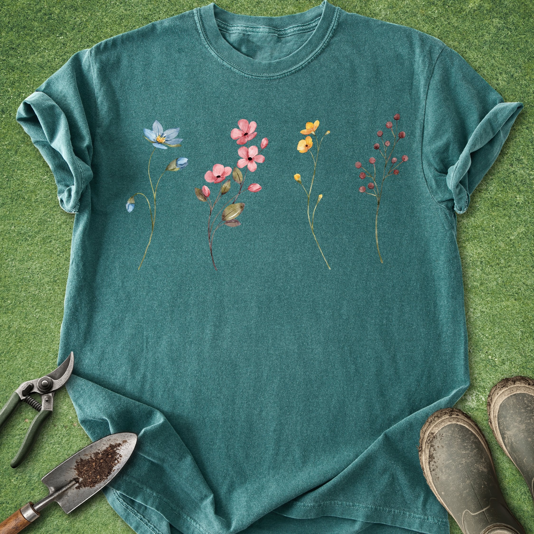Teal t-shirt with floral designs on a grassy background