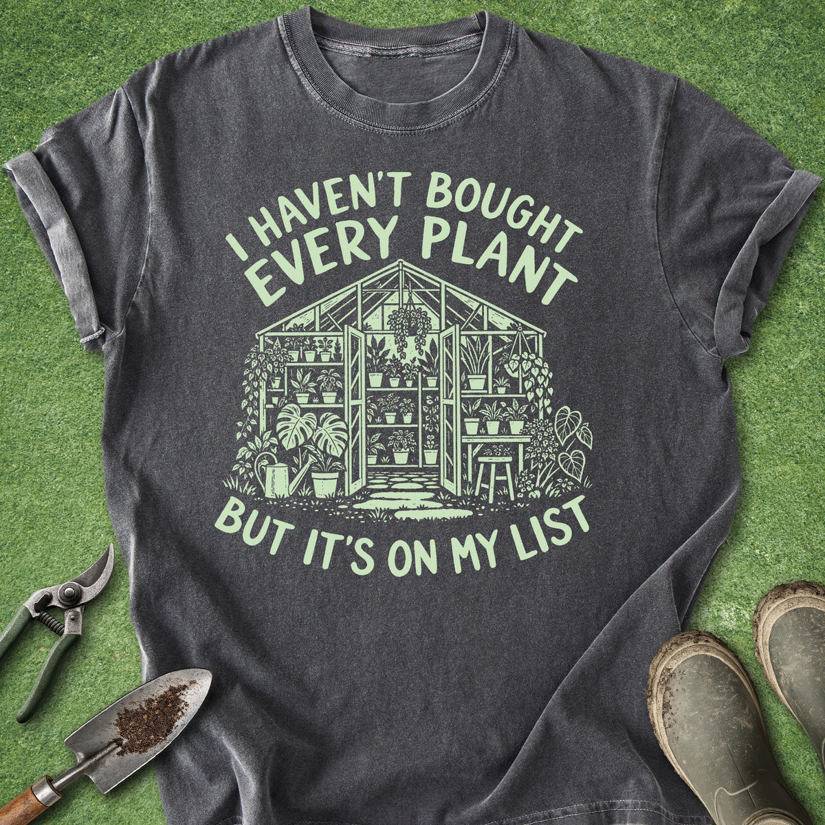 Dark gray plant lover shirt featuring a greenhouse filled with plants and the saying I Haven’t Bought Every Plant But It’s On My List.