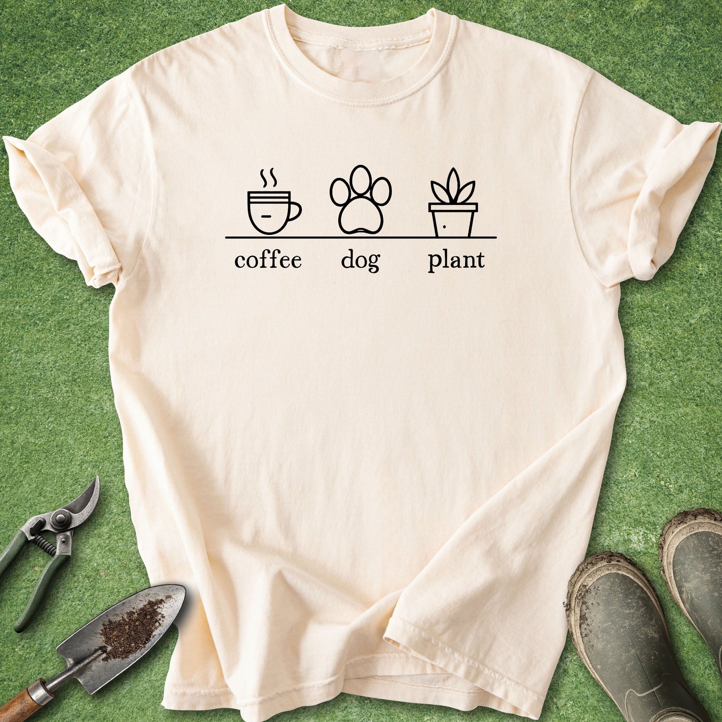 Beige t-shirt with 'coffee', 'dog', and 'plant' graphic on a green grass background