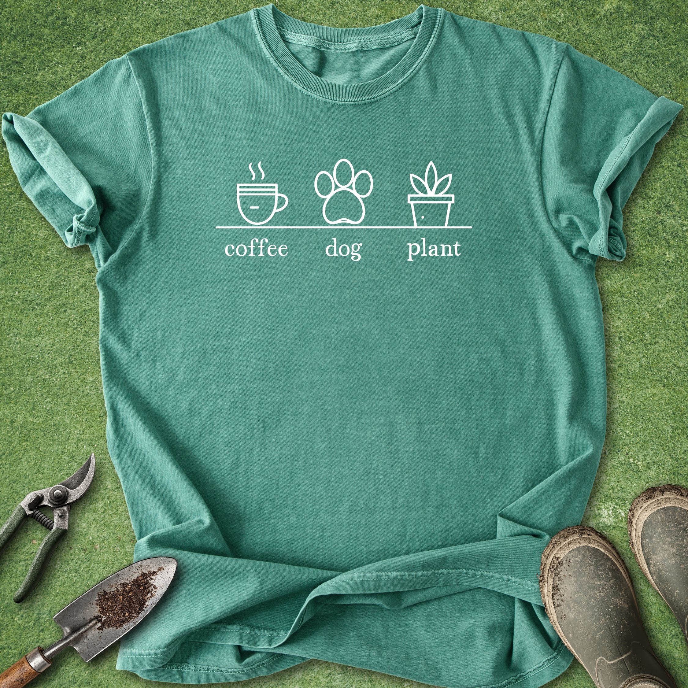 Green t-shirt with 'coffee', 'dog', and 'plant' design on a grass background