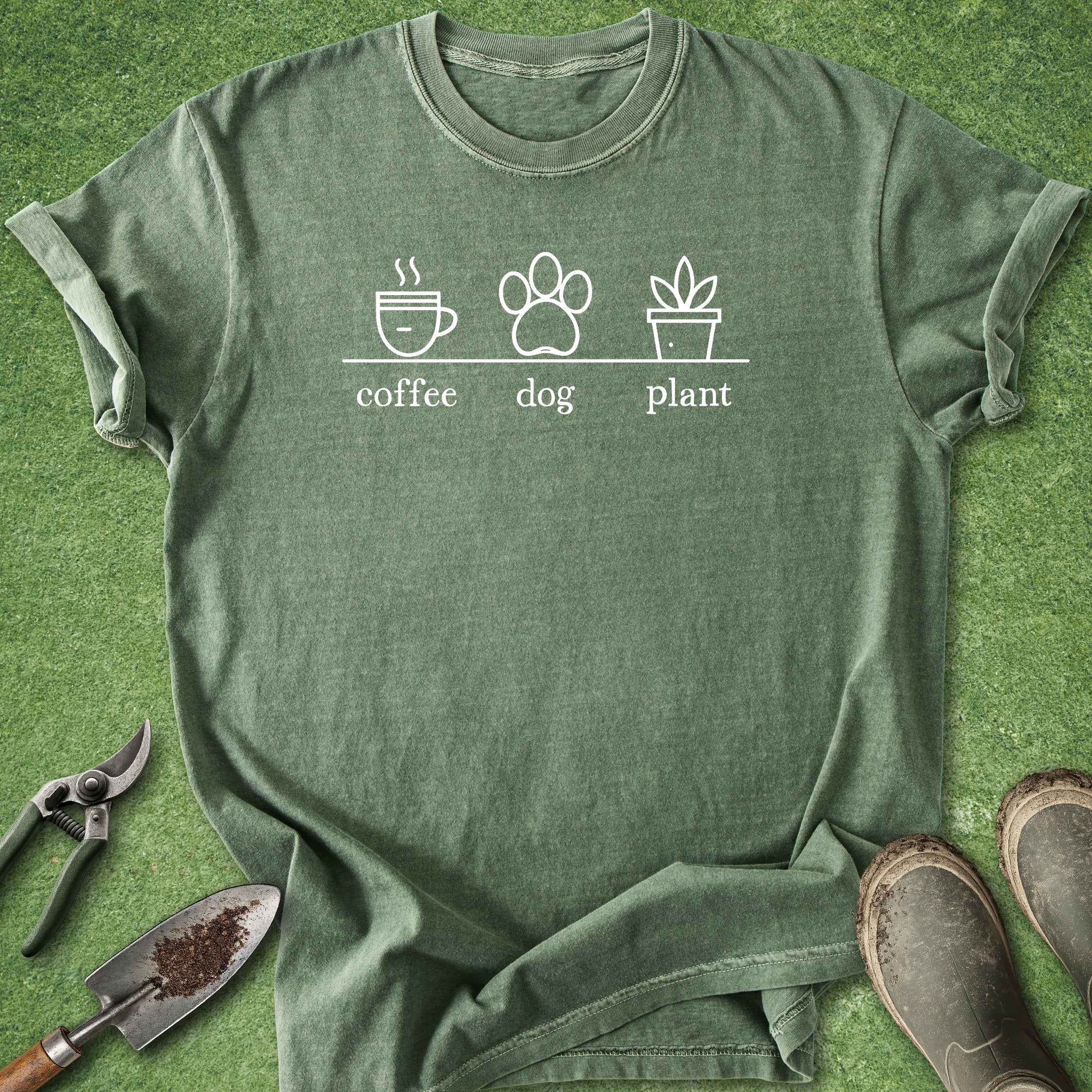 Green t-shirt with 'coffee', 'dog', and 'plant' graphic on a grass background